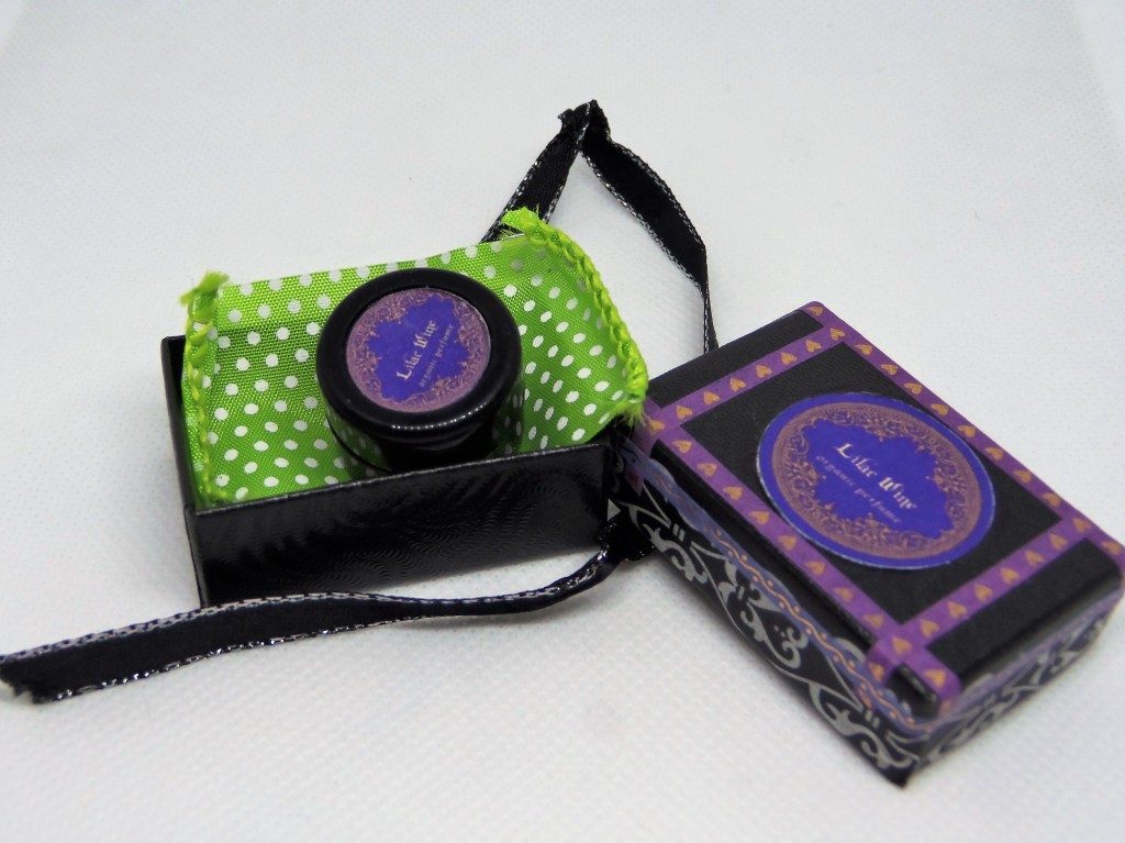 The Lilac Wine box, open, with the perfume inside, atop a green ribbon. The box was tied with a black and silver ribbon.