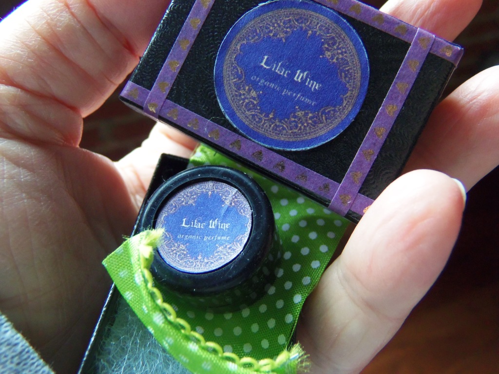The Lilac Wine solid perfume box, opened, to show the perfume resting on a green and white ribbon